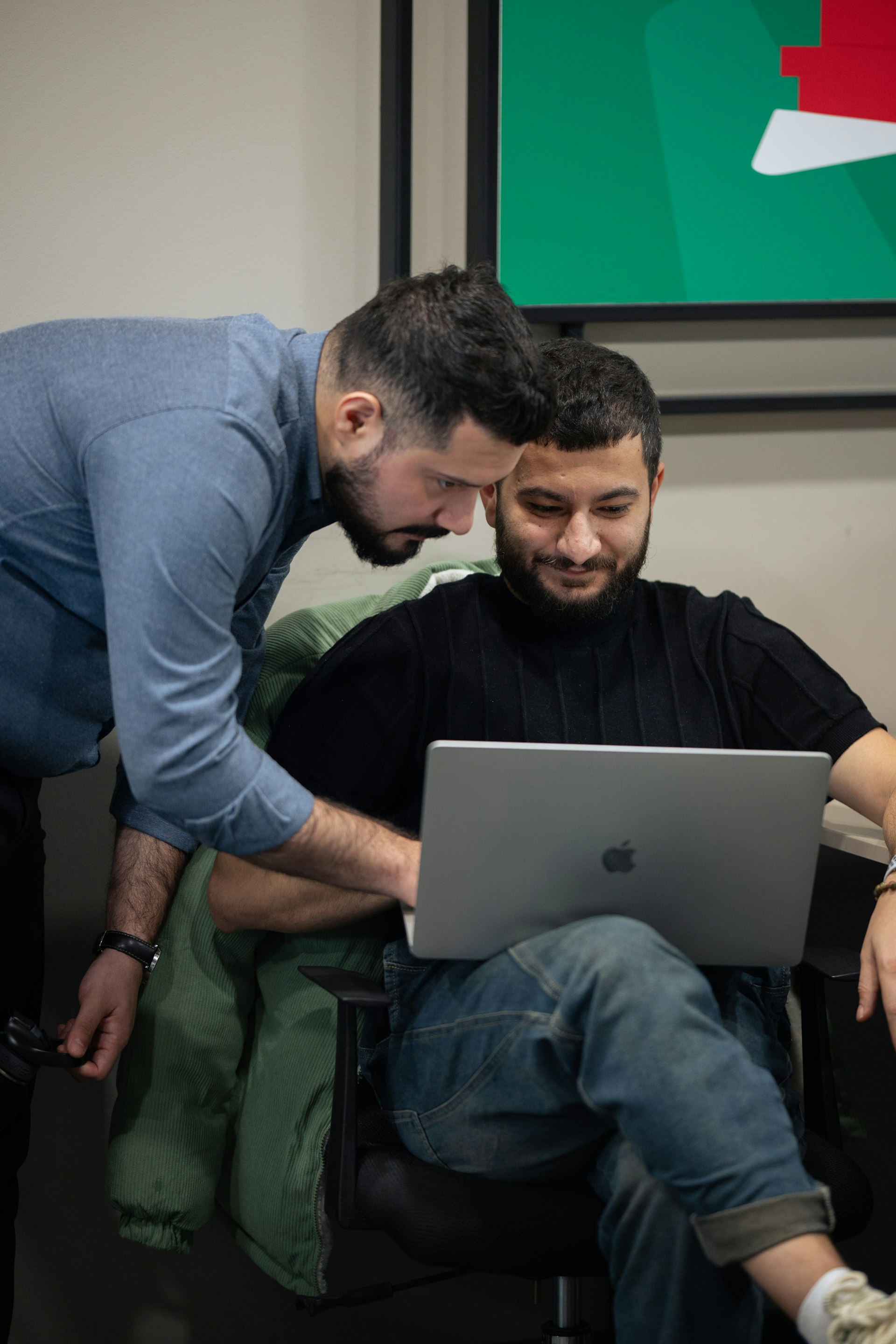 One person leaning in to help another with a laptop